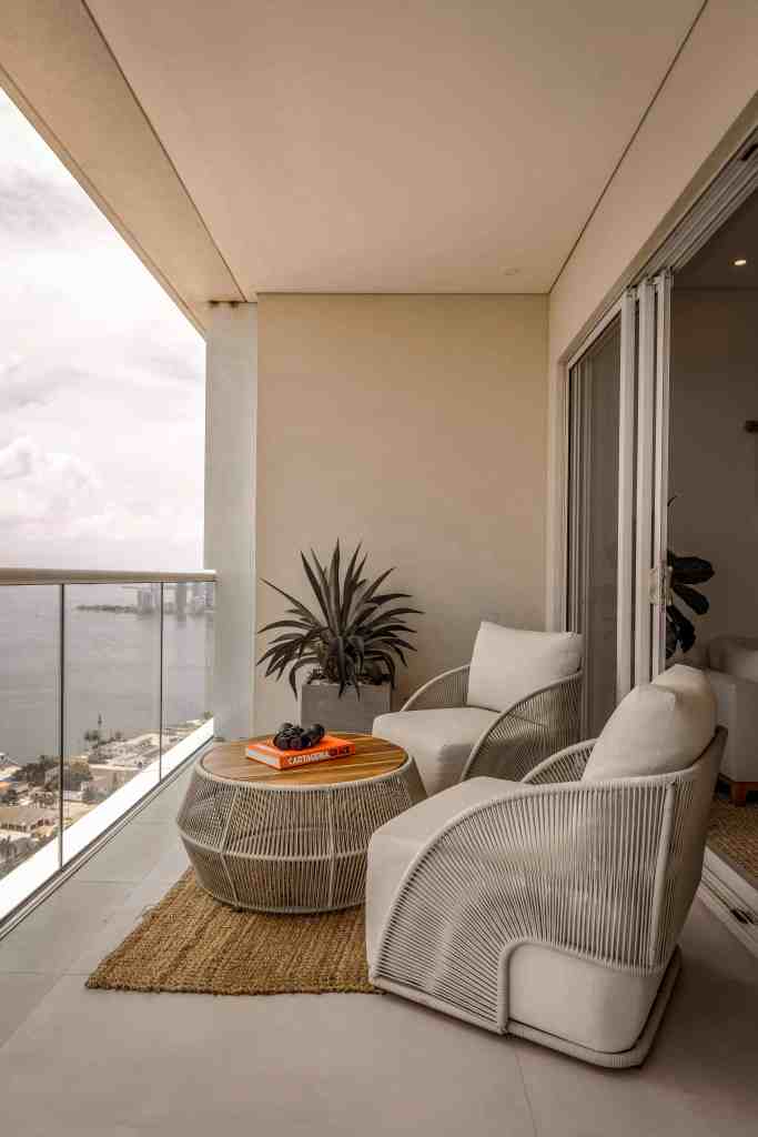 A stylish balcony with two modern chairs and a round table, overlooking a scenic view of the water and cityscape, featuring a potted plant and decorative items.