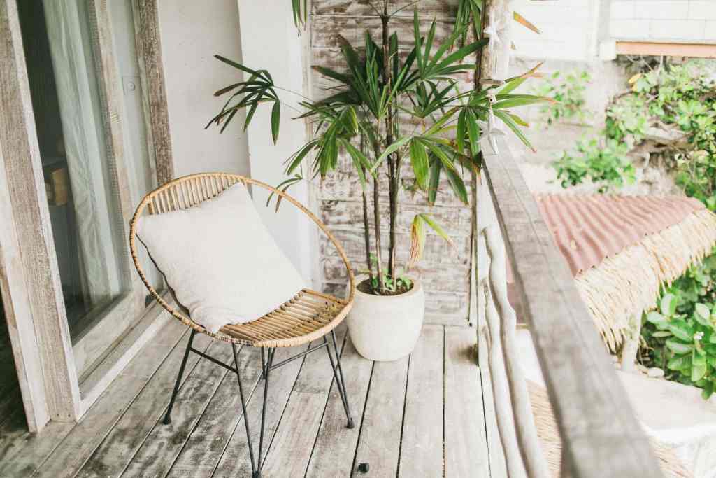 A cozy balcony featuring a rattan chair with a cushion, accompanied by a potted plant and wooden flooring.